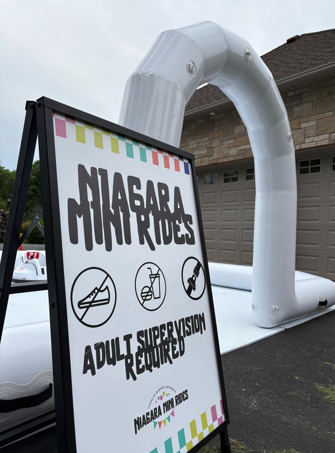 Our signature all-white bumper car set up. Perfect for driveways and event spaces. Niagara Mini Rides white bumper car arena setup in driveway with inflatable border and signage.